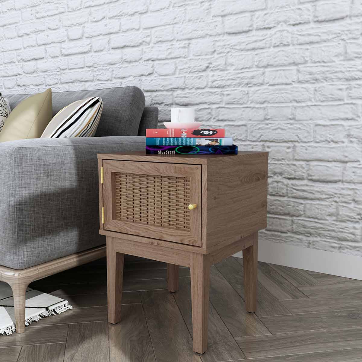 Brown wooden lamp table with a woven rattan door, featuring a sleek design and gold handle, positioned beside a gray sofa against a white brick wall.