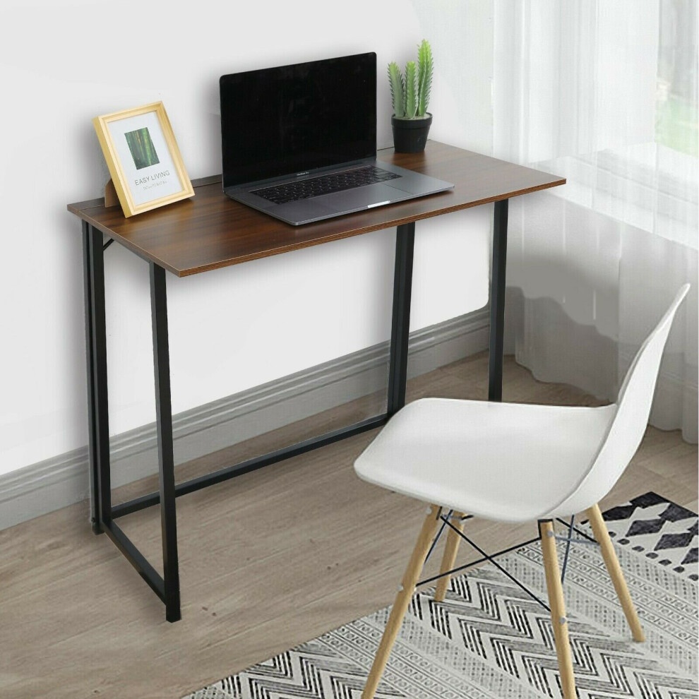 Brown folding computer study desk with a wooden top, black metal legs, a laptop on the surface, a small plant, and a framed picture, accompanied by a white chair.