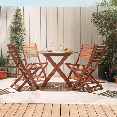 Brown wooden octagonal table with a slatted top and four matching folding chairs, set in a garden with greenery and potted plants in the background.