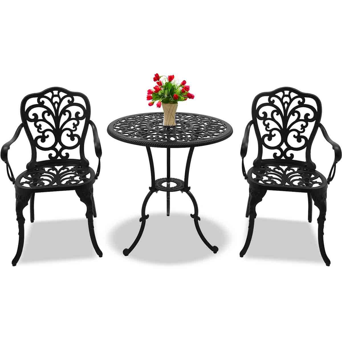 Black cast aluminium bistro set featuring an intricately designed table and two matching chairs, complemented by a small vase of red flowers on the table.