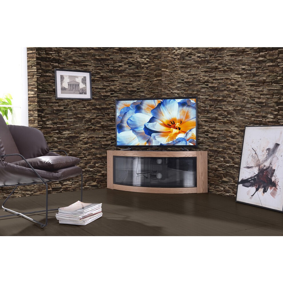 Curved oak TV cabinet with a glass front, accommodating 32"-55" TVs, set against a textured stone wall, complemented by modern artwork and a sleek black chair.