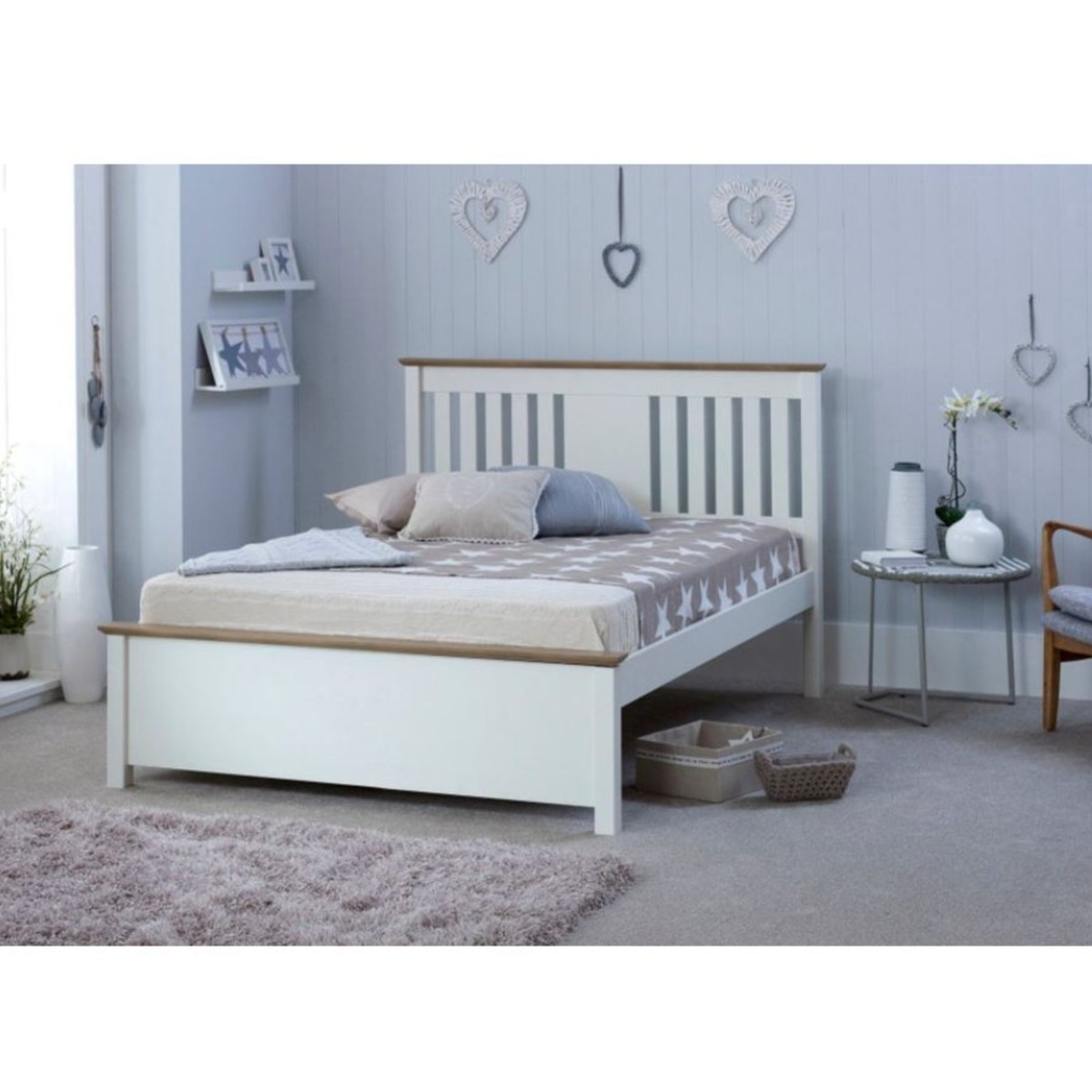 White wooden double bed with a slatted headboard and light wood accents, complemented by a neutral-toned quilt and a cozy room setting with decorative hearts.