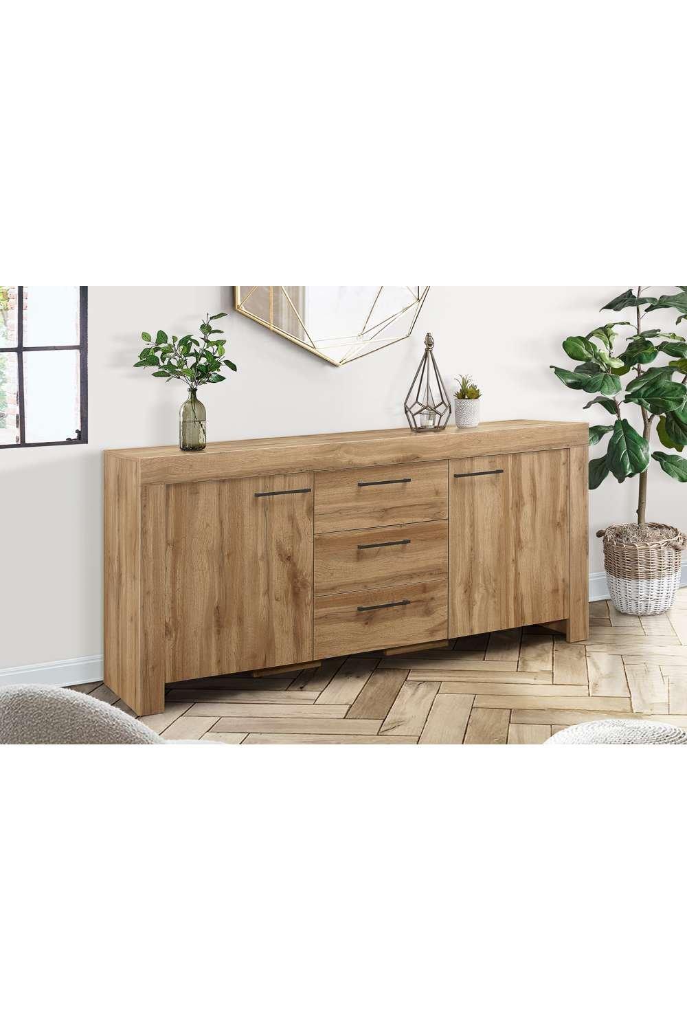 Brown oak sideboard featuring three drawers and two doors, with a sleek design, complemented by decorative plants and a geometric mirror in a well-lit room.