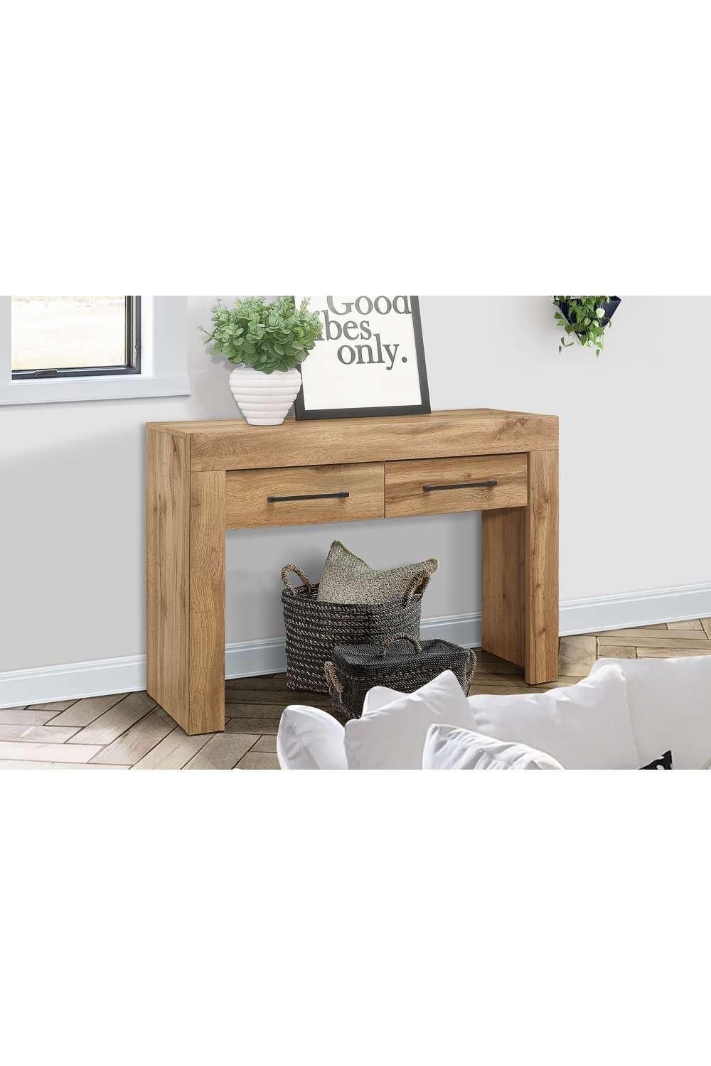 Brown oak console table with two drawers, a spacious top, and an open shelf underneath, complemented by a decorative plant and framed artwork in a bright interior setting.