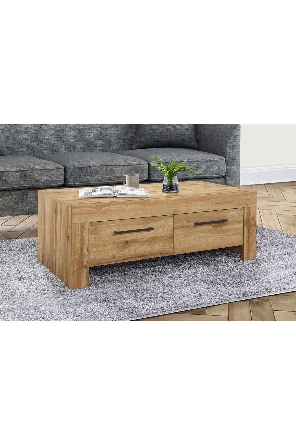 Brown oak coffee table with four drawers, featuring a sleek design and metal handles, placed on a textured gray rug in a living room setting.