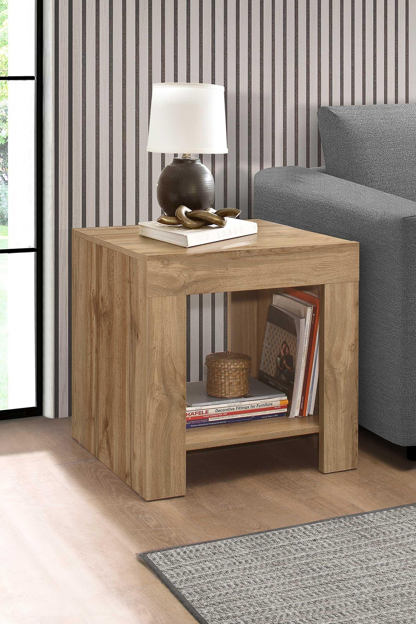 Brown wooden side table with a minimalist design, featuring an open shelf for storage, placed beside a gray sofa and a lamp on top.