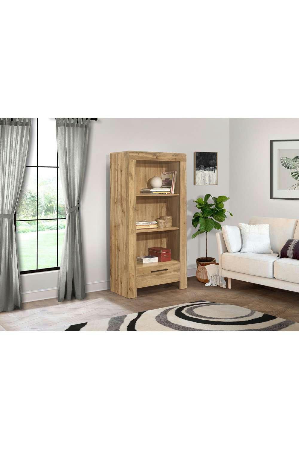 Brown oak bookcase with a drawer, featuring three open shelves, set against a light-colored wall with a cozy living room backdrop, including a plant and a sofa.