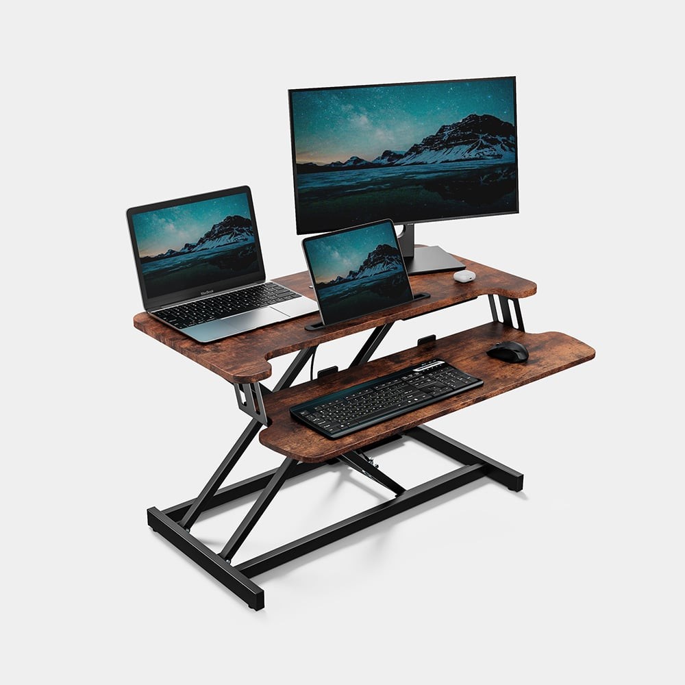 Dark wood standing desk converter with a two-tier design, featuring a top shelf for a monitor and a lower shelf for a laptop, supported by a sturdy black metal frame.