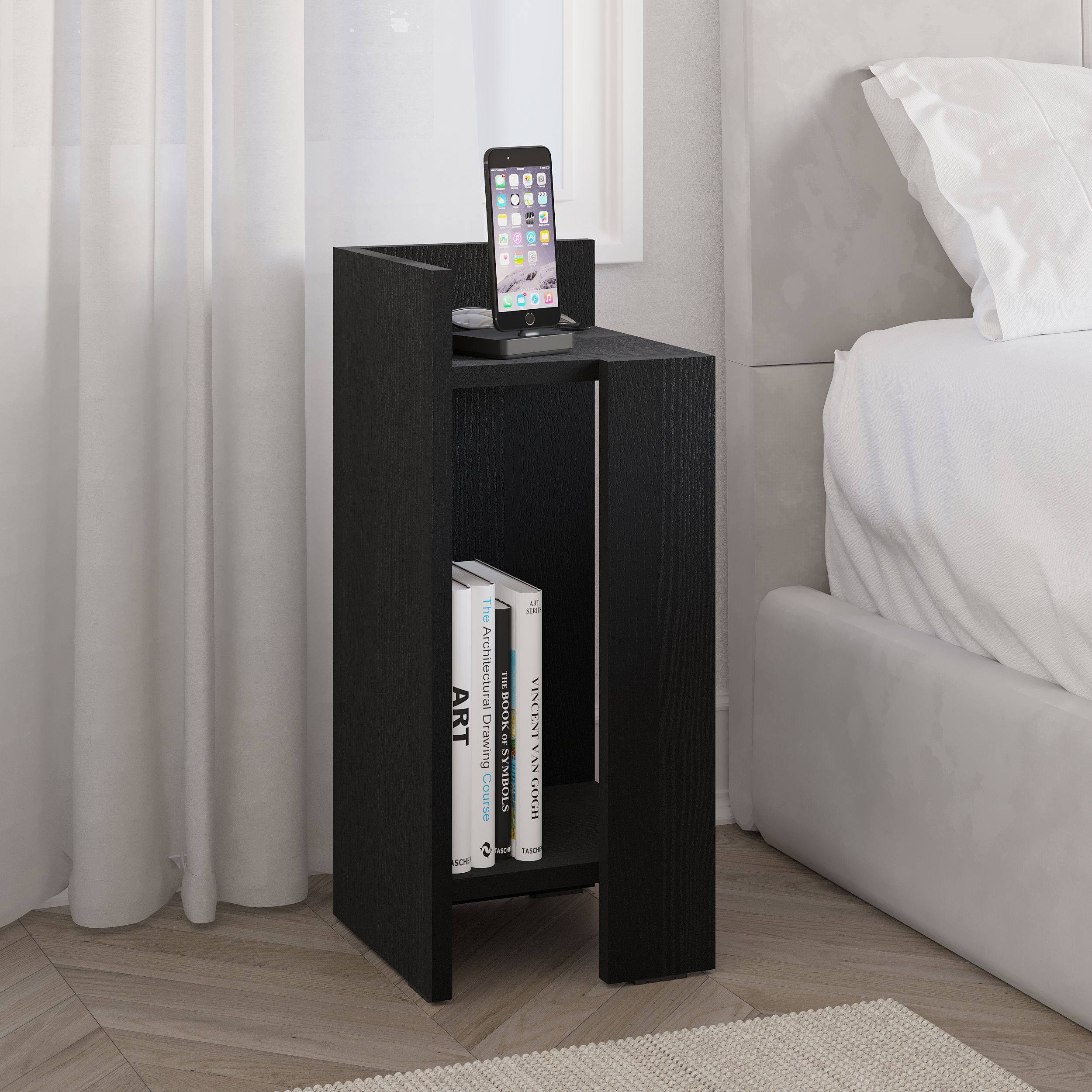 Black particleboard bedside table with a sleek design, featuring a top shelf for a phone and two lower shelves for books, positioned beside a bed with light bedding.