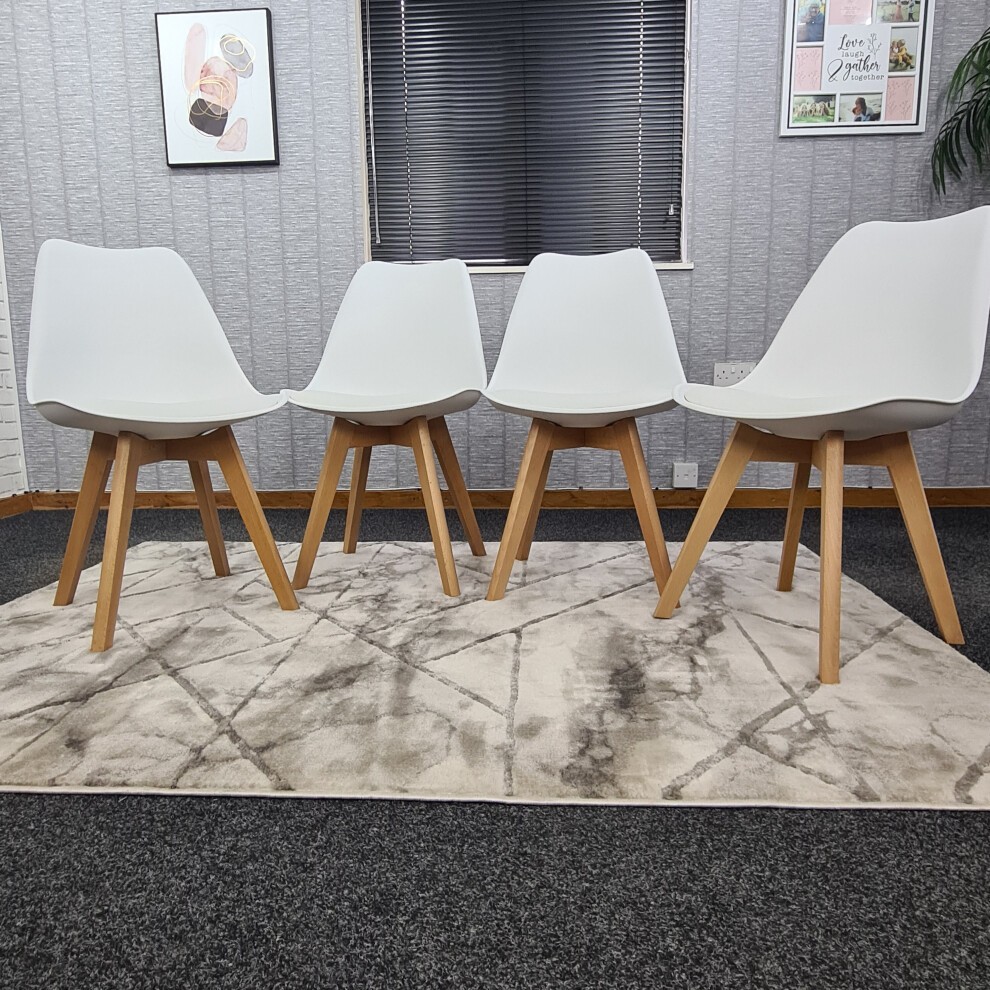 Four white tulip chairs with a smooth, molded plastic seat and natural wood legs arranged in a modern interior setting on a patterned rug.