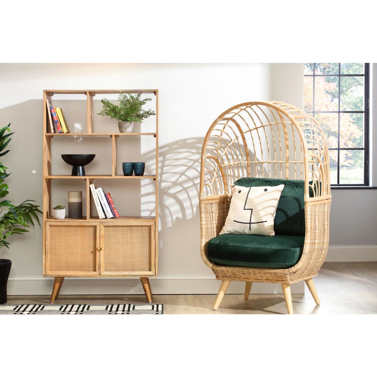 Natural rattan bookshelf with open and closed storage, featuring a light wood finish, six shelves, and a cabinet, alongside a rattan chair with green cushions.