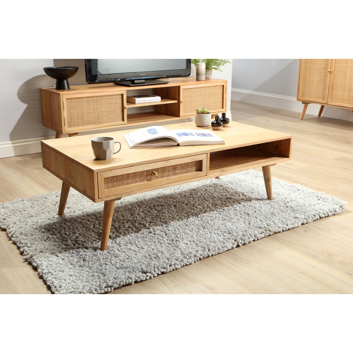 Natural wood coffee table with a cane drawer, tapered legs, and a smooth surface, placed on a textured rug, complementing a modern living room setting.