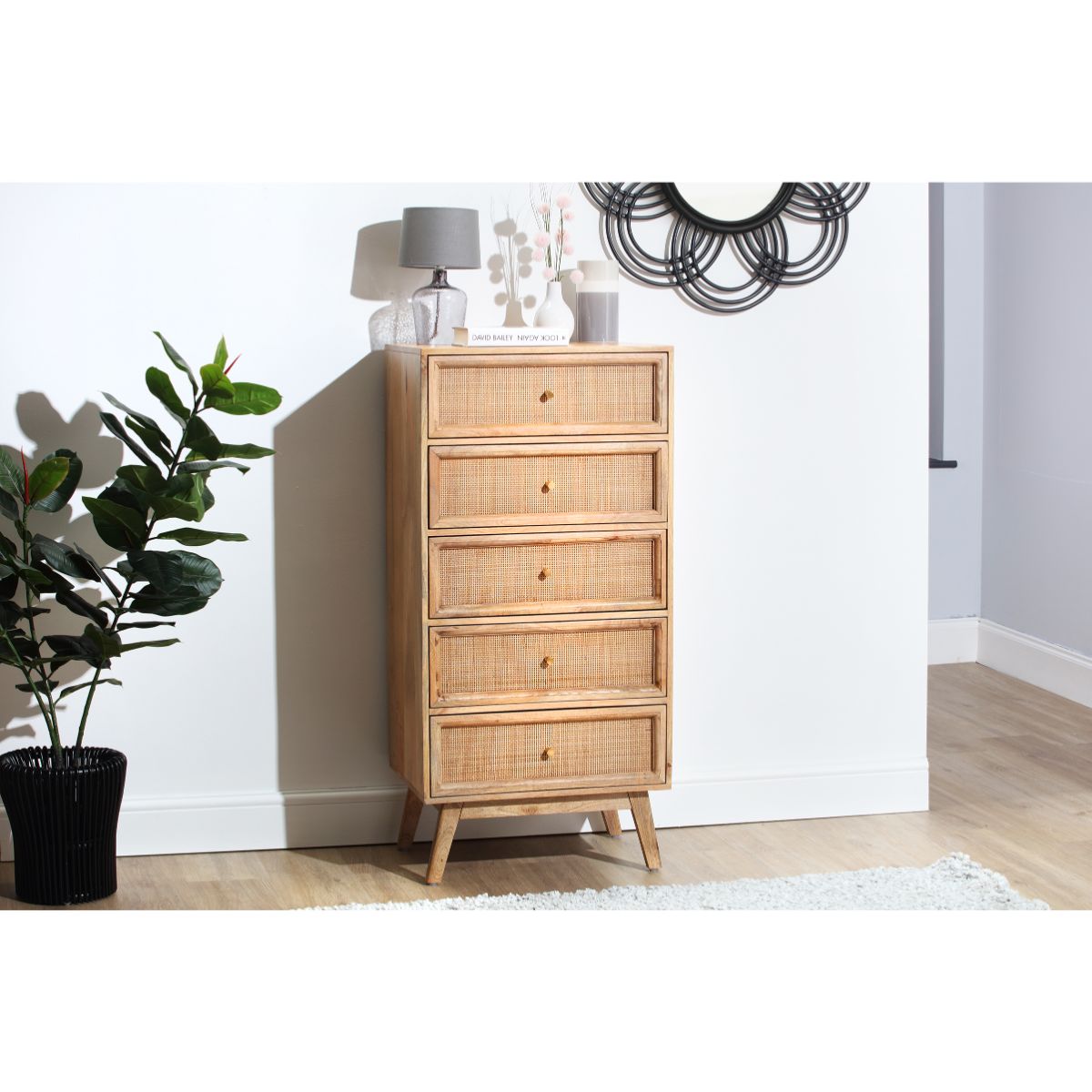 Natural rattan drawer unit with five tall drawers, light wood finish, round wooden knobs, and tapered legs, complemented by a decorative mirror and lamp in a modern setting.