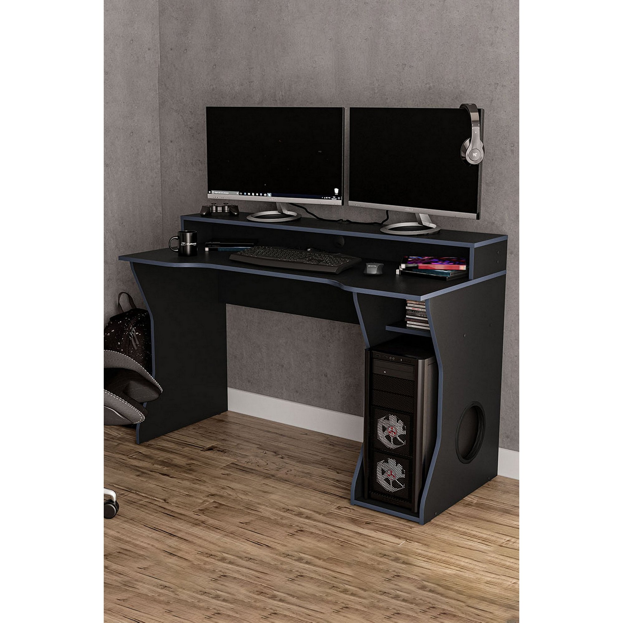 Birlea Enzo Gaming Computer Desk features a dark blue finish, sleek design, dual monitor setup, keyboard tray, and a stylish cutout for cable management, set against a textured wall.