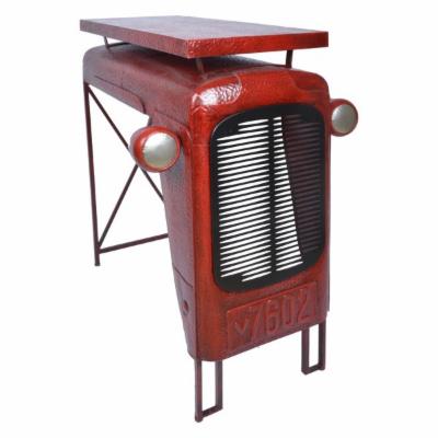 Red metal table designed to resemble a vintage tractor, featuring a textured surface, grill-like front, and sturdy black legs for an industrial aesthetic.