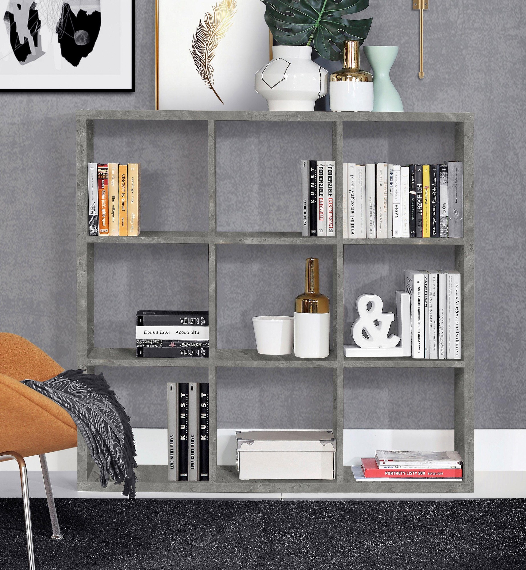 Gray concrete-style 3x3 storage unit featuring nine open compartments, styled with books, decorative vases, and a modern ampersand, set against a textured wall.
