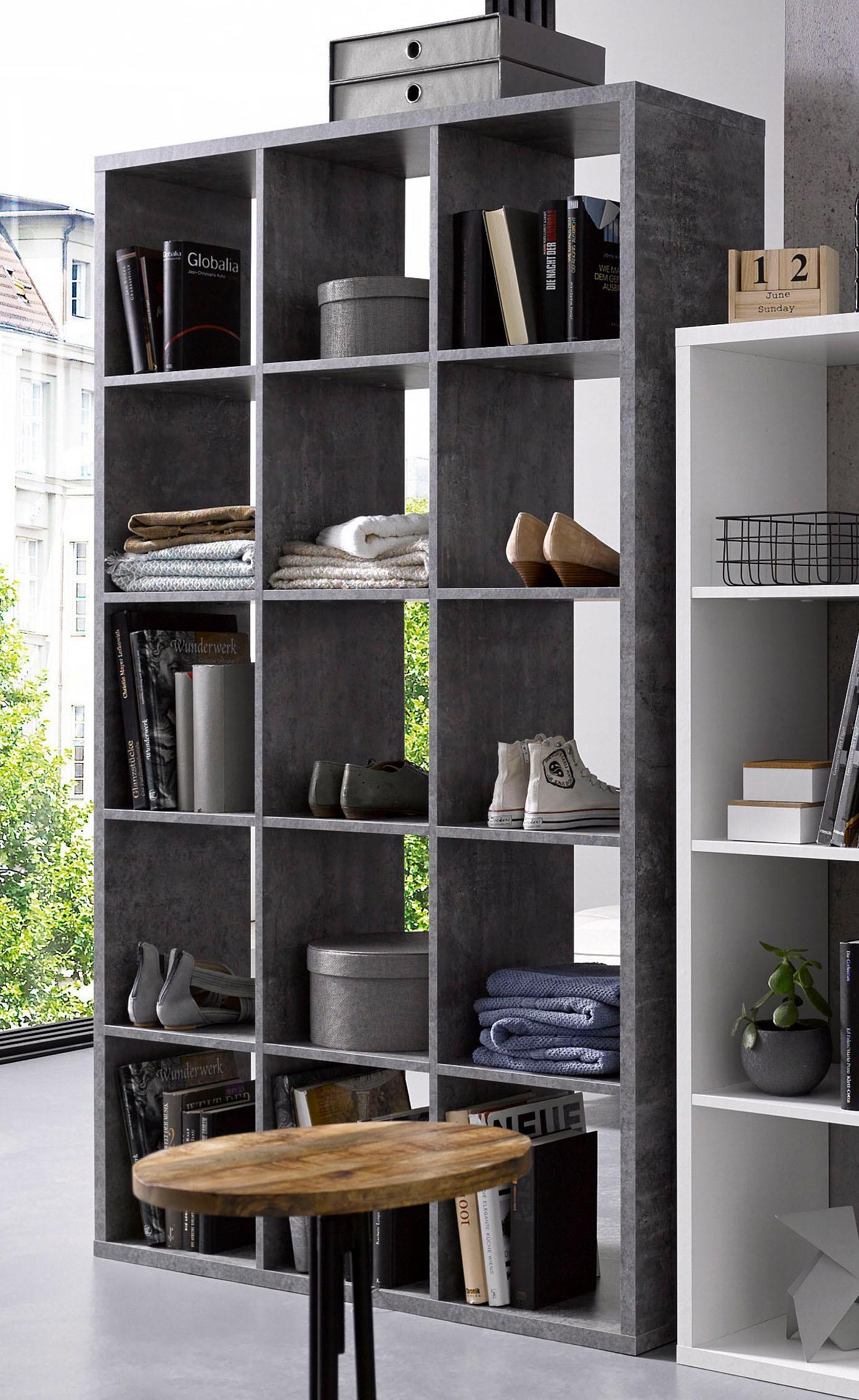 Gray, modern 3x5 storage unit with open cubbies, featuring books, shoes, and decorative boxes, complemented by a round wooden table in the foreground.