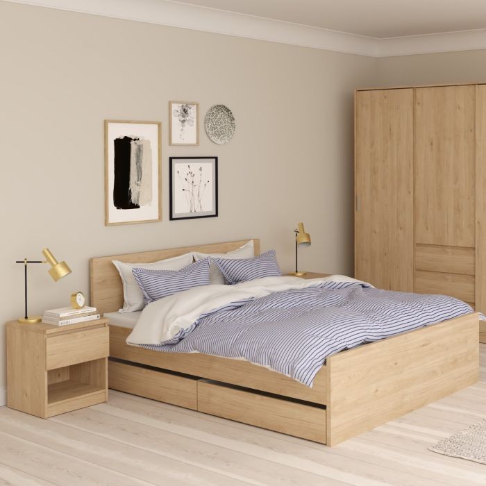 Naia Bedside table in light wood finish features one drawer and an open shelf, complementing a modern bedroom with a cozy bed and stylish decor.