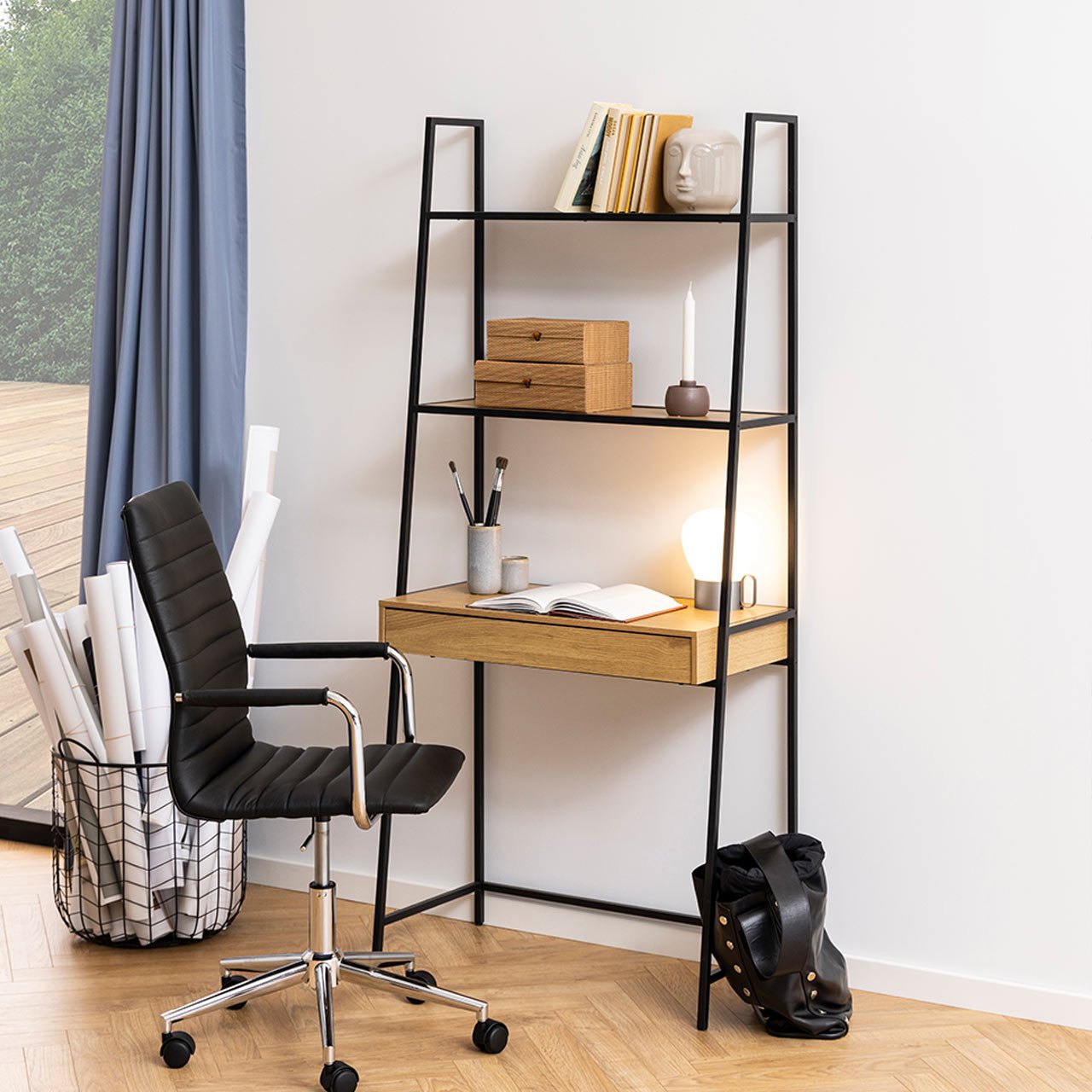 Seaford Bookcase featuring a black metal frame and oak drawer, with three open shelves, a stylish desk area, and a modern lamp, complemented by a sleek black office chair.