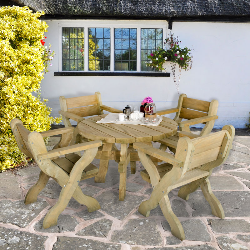Circular wooden garden table in natural wood finish, measuring 4'x4', with four matching folding chairs, set on a stone patio near a cottage with flowering plants.