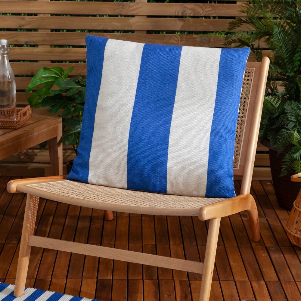 Blue and white striped woven outdoor cushion resting on a wooden chair, surrounded by greenery and wooden decking, showcasing a vibrant and durable fabric.