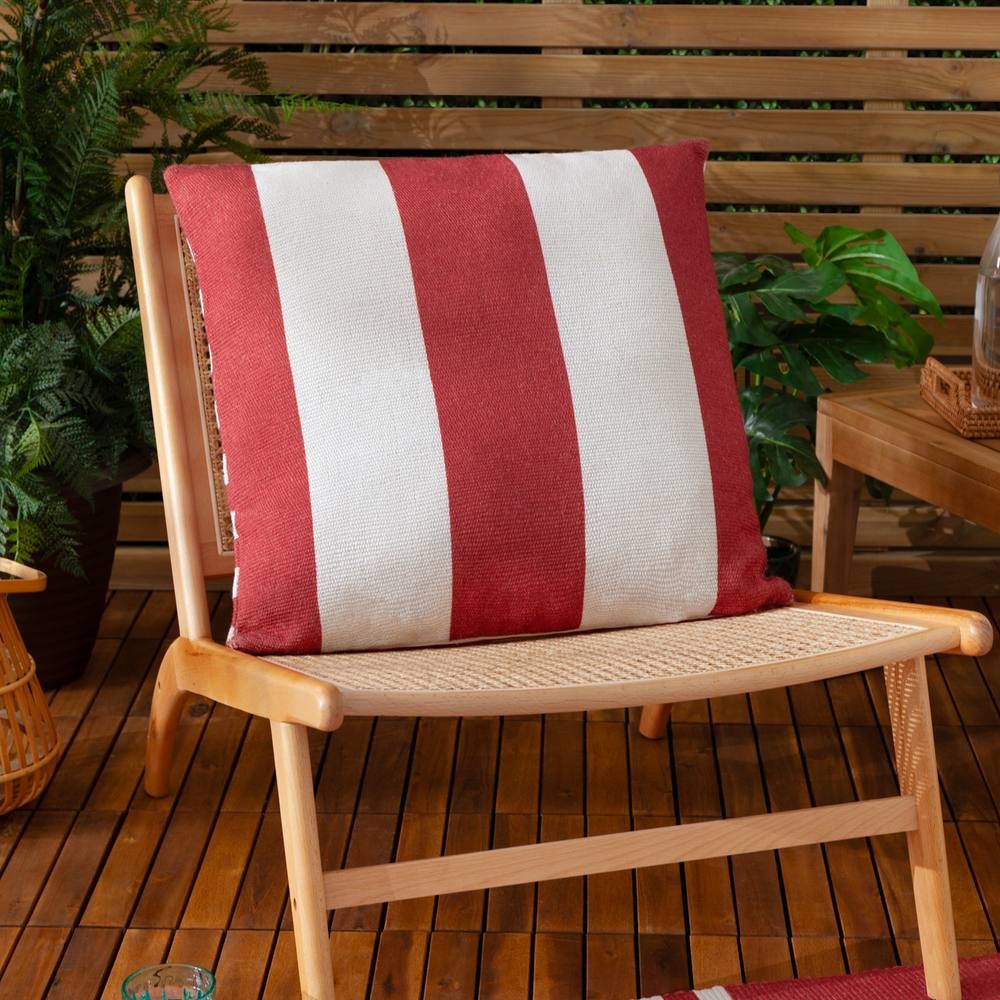 Red and white striped woven outdoor cushion featuring a textured fabric, positioned on a wooden chair with a natural setting of plants and decor in the background.