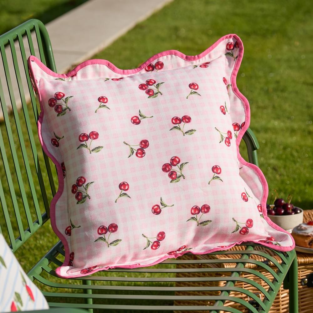 Pink outdoor cushion featuring a gingham check pattern with cherry motifs, scalloped edges, and a soft fabric, perfect for adding a pop of color to outdoor spaces.
