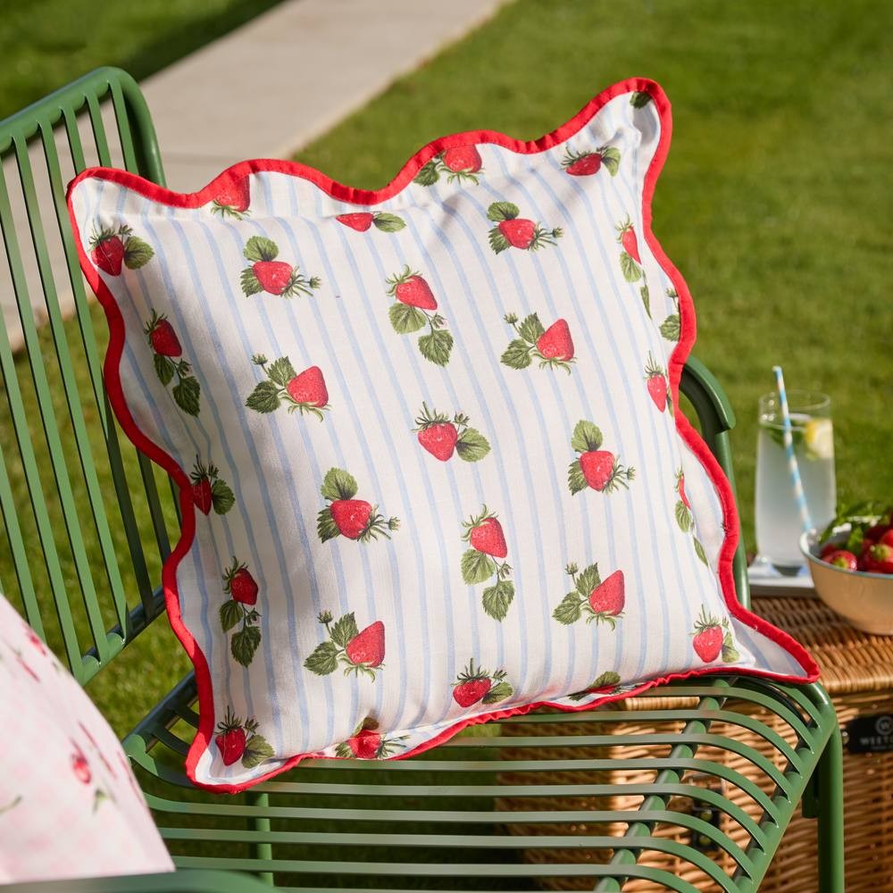 Blue striped outdoor cushion featuring a strawberry print and red scalloped edges, made from durable fabric, perfect for adding a pop of color to outdoor seating.