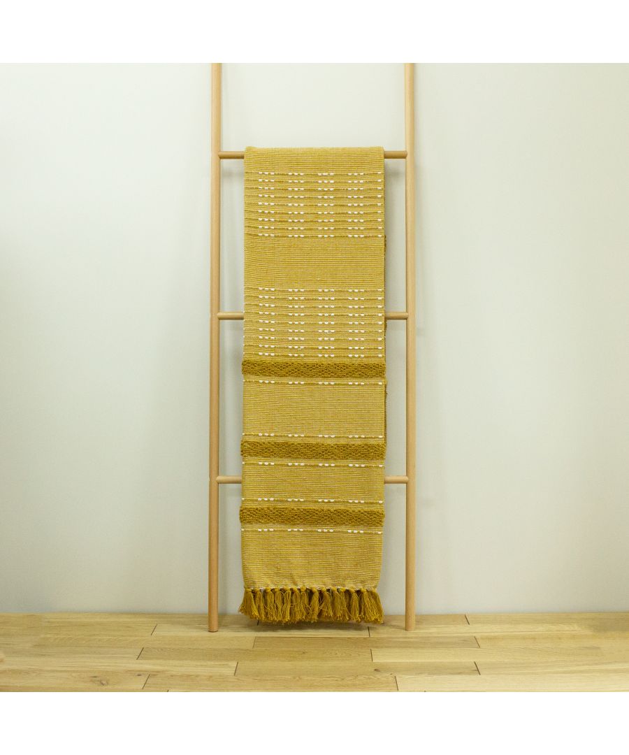 Ochre yellow cotton throw with textured patterns and fringed edges, hanging on a wooden ladder against a light background.