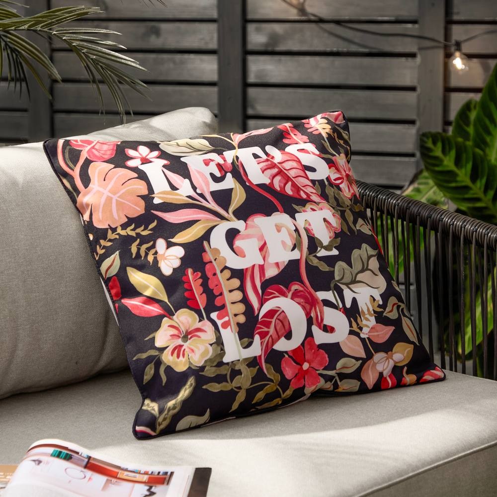 Black outdoor cushion featuring vibrant tropical floral patterns in red, pink, and green, with the phrase "LET'S GET LOST" prominently displayed in white.