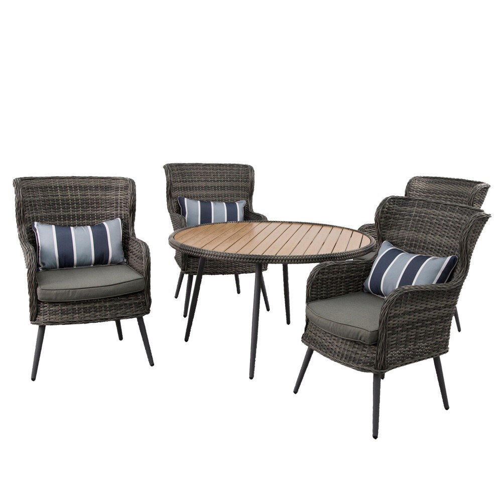 Luxury rattan dining table set featuring a round wooden tabletop and four cushioned chairs with striped pillows, all in a stylish dark grey finish.