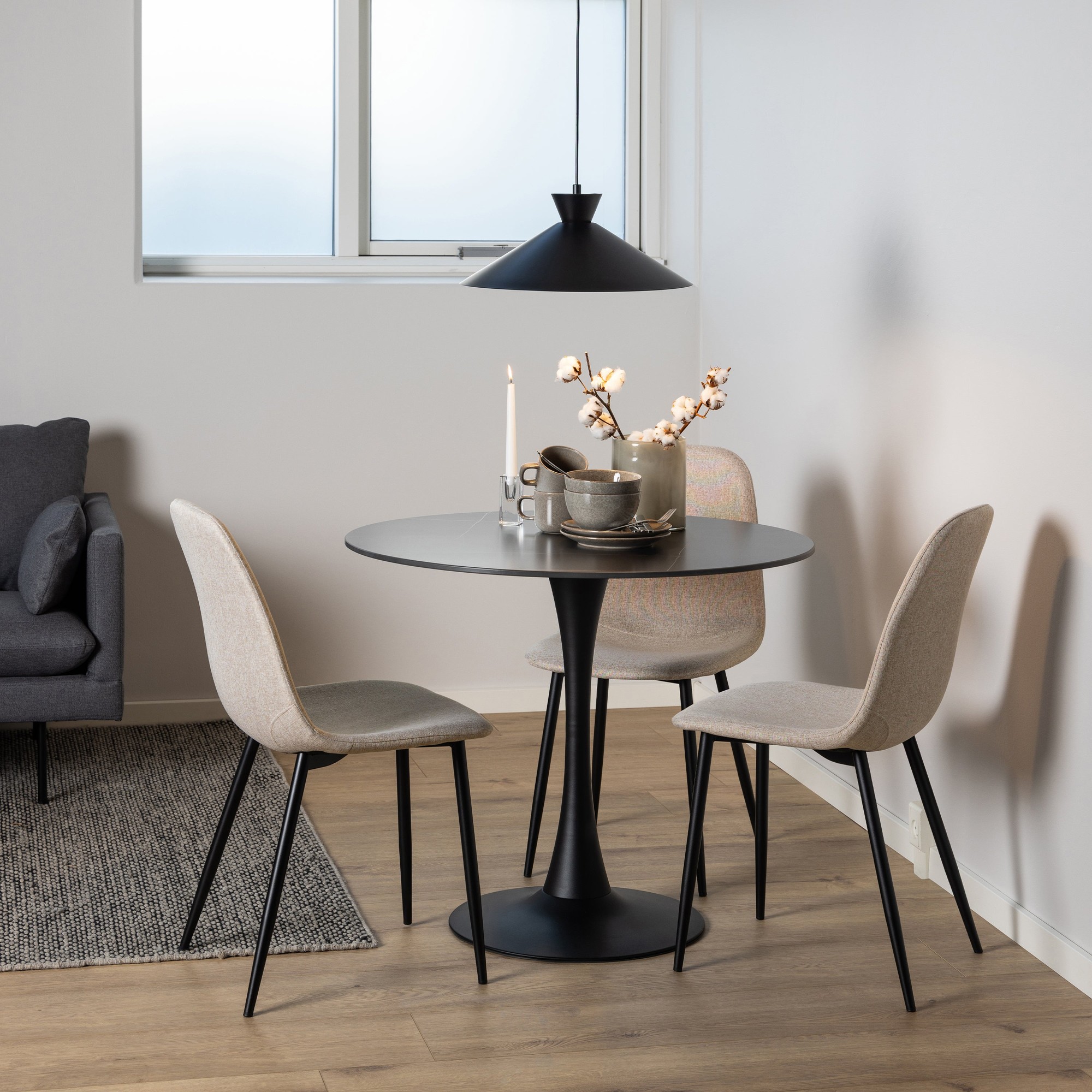 Light grey upholstered dining chairs with black metal legs, arranged around a round black table, complemented by a minimalist pendant lamp and decorative table setting.