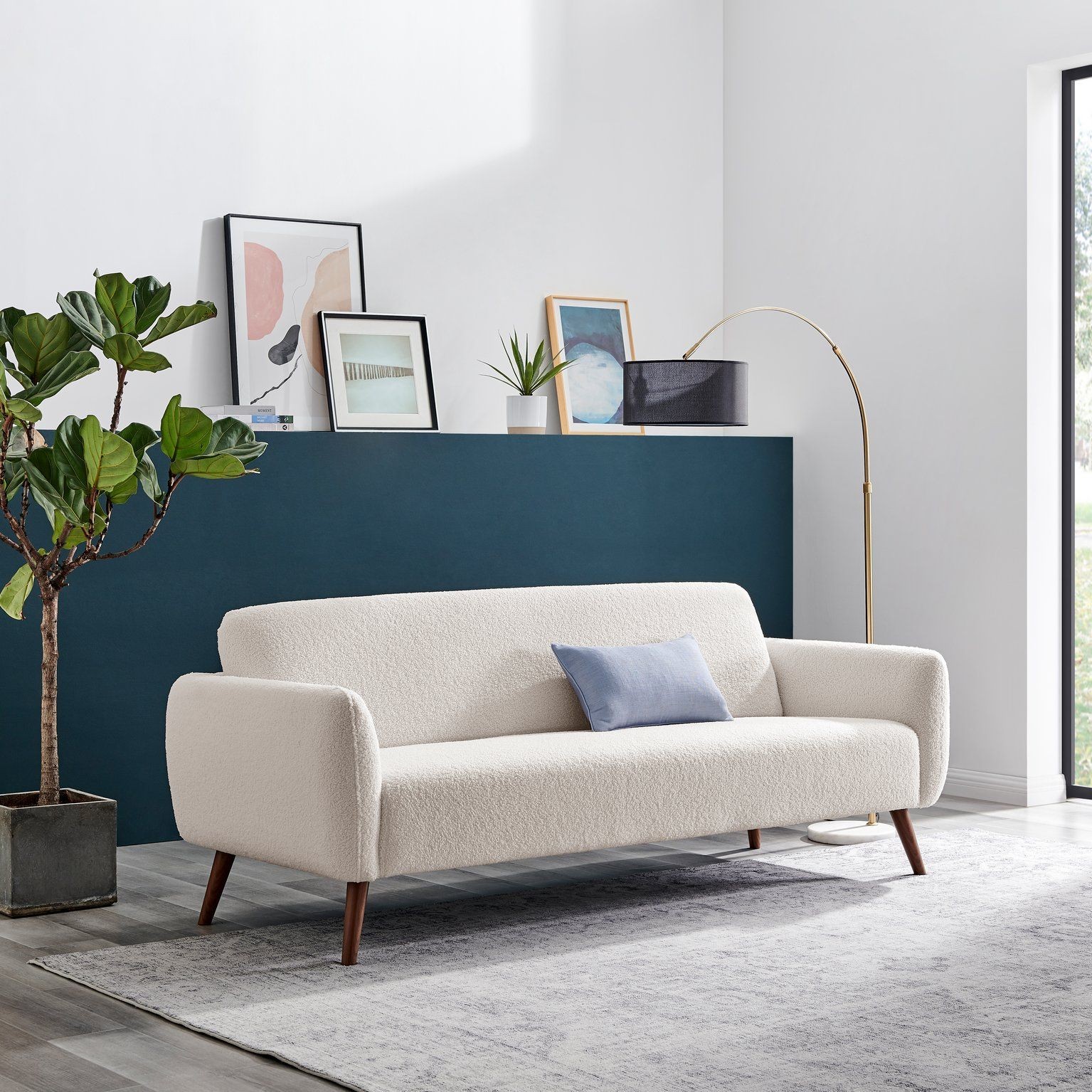 White teddy soft boucle fleece retro sofa with a minimalist design, featuring rounded arms, wooden legs, and a small blue cushion, set against a modern interior backdrop.