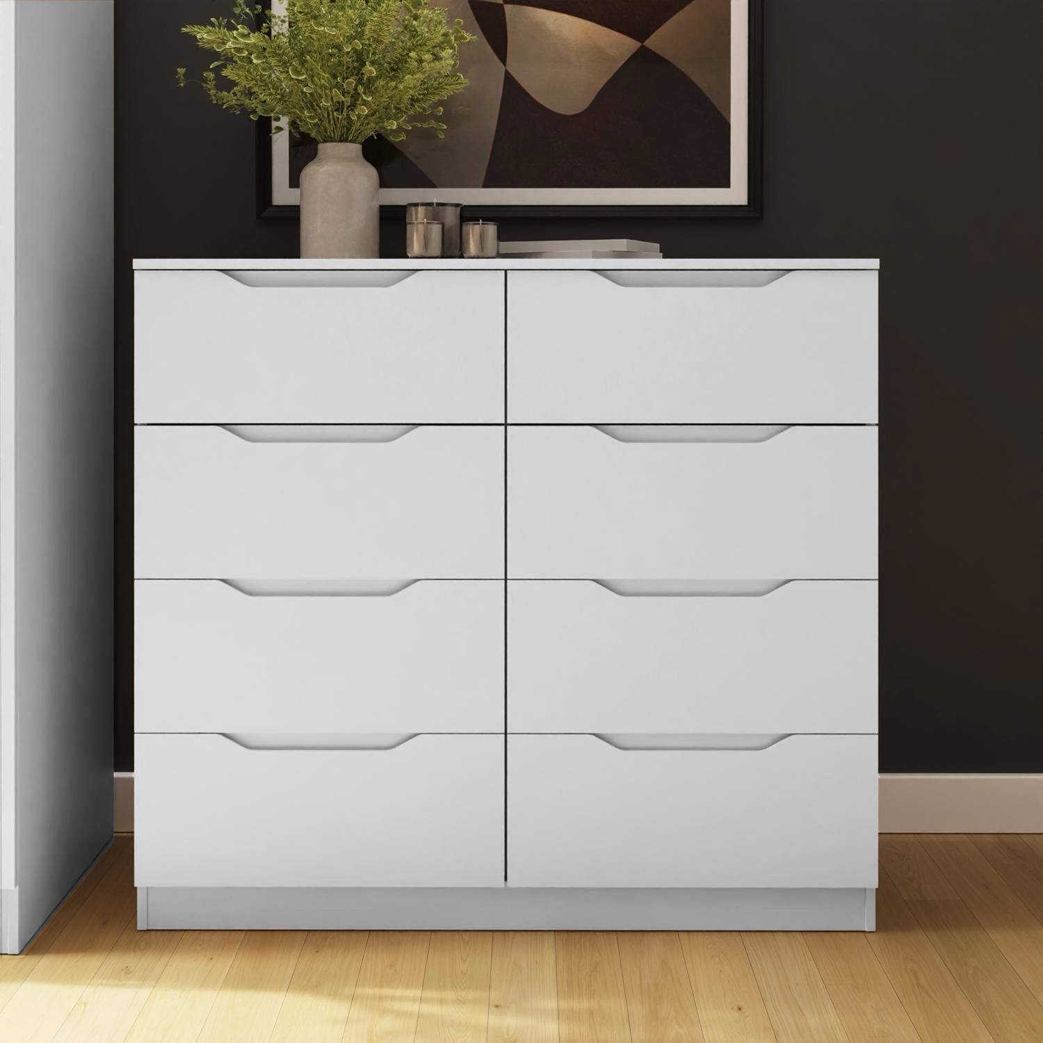 Modern wide chest of drawers in white with eight spacious drawers featuring sleek handles, set against a dark wall, complemented by a vase of greenery and abstract art.