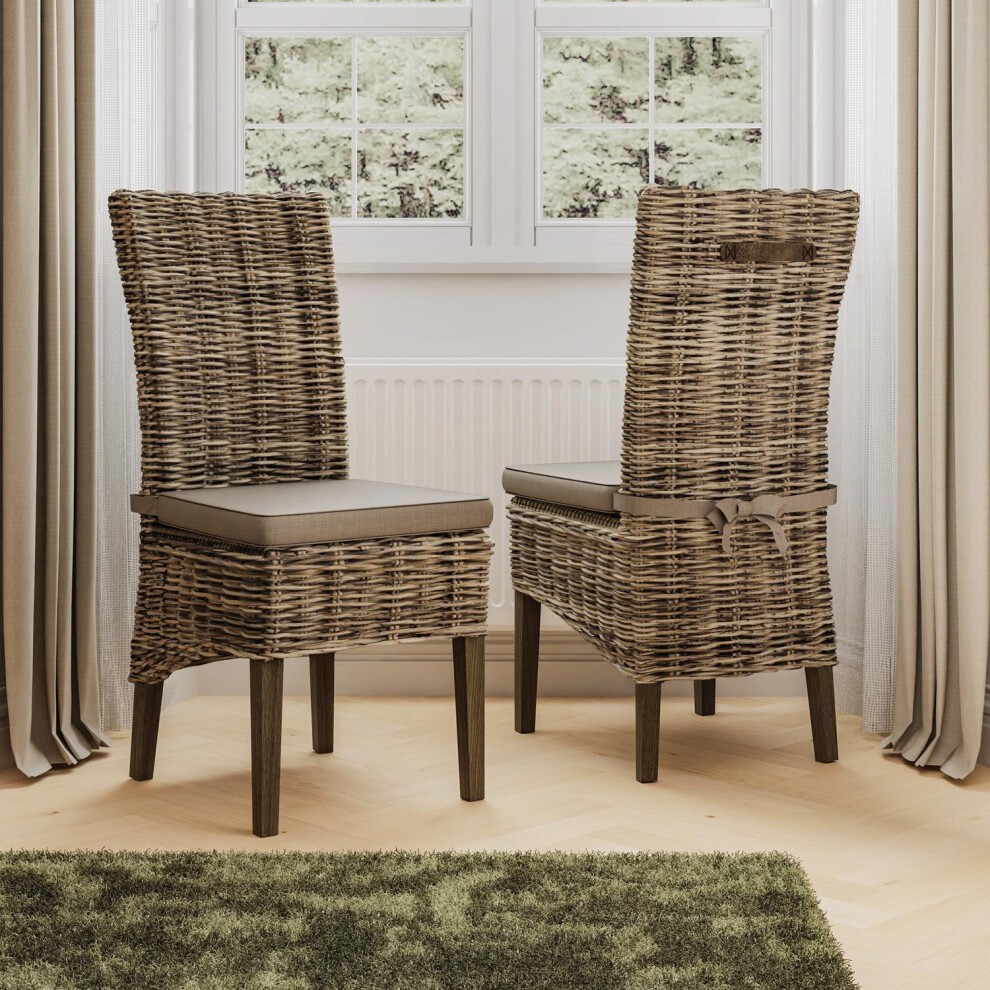 Set of 2 solid pine dining chairs featuring a greywash finish, rattan weaving, and cushioned seats, positioned near a window with curtains and a green rug.
