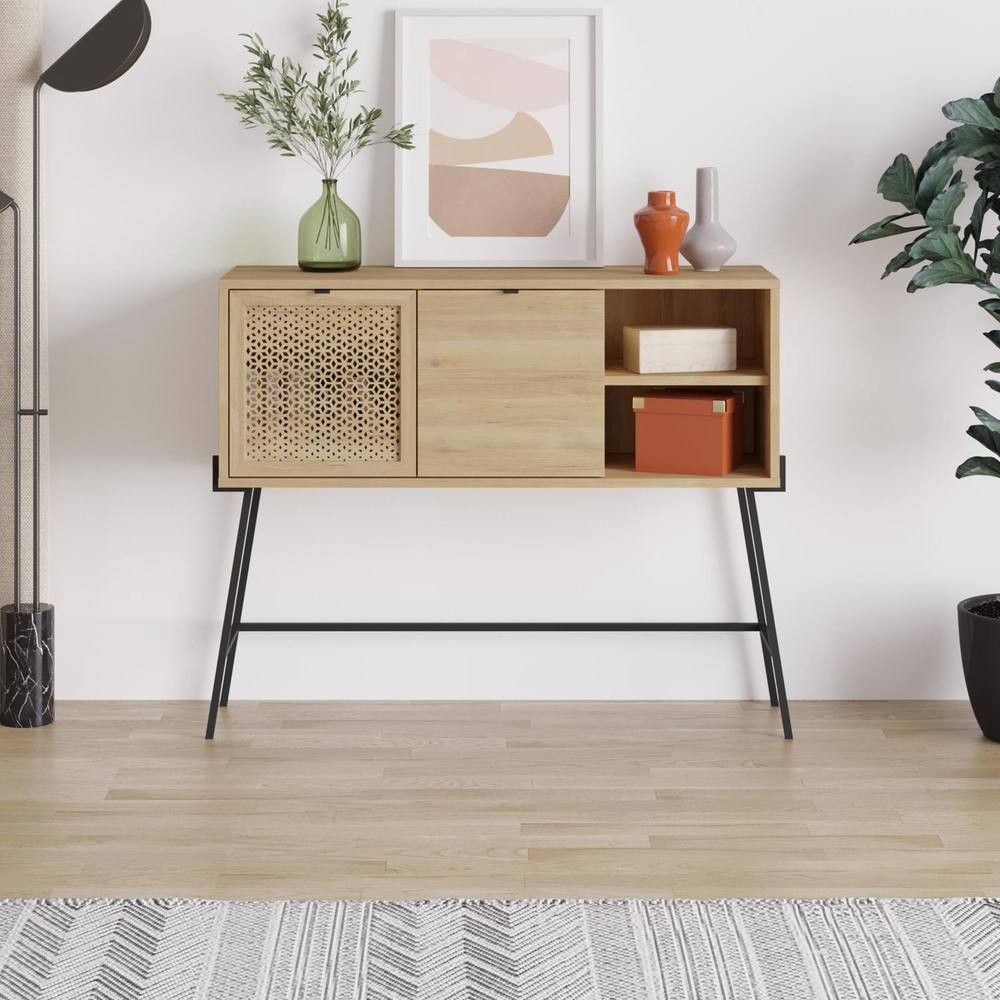 Naive 2 Door Sideboard in Sapphie Oak effect with a metal frame, featuring one open shelf, one closed compartment, and a decorative woven door, set against a light wooden floor.