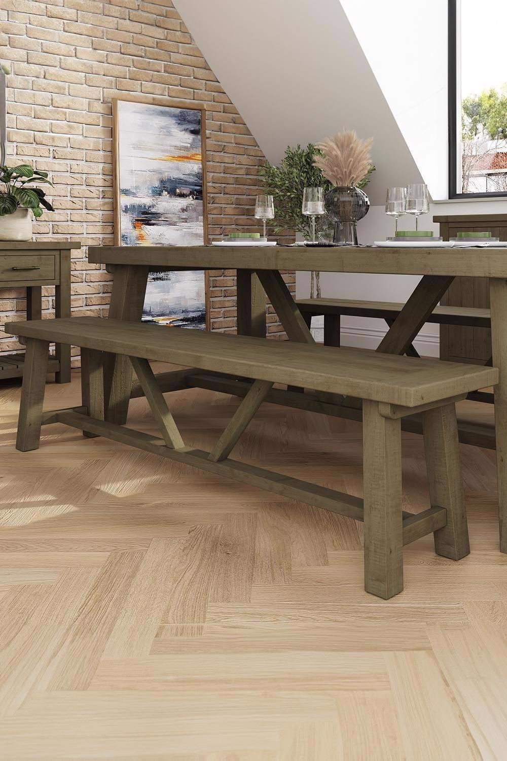 Reclaimed pine dining bench in brown with a rustic finish, featuring a sturdy X-frame design, placed in a bright room with a wooden floor and decorative elements.