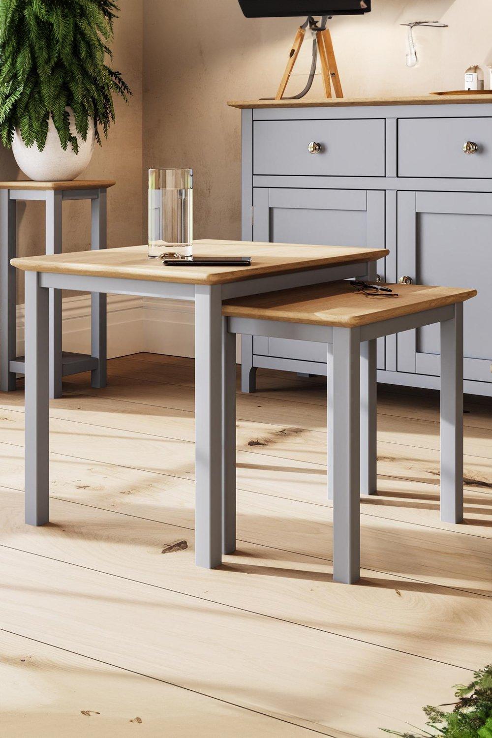 Grey ready-assembled nest of 2 tables featuring a natural wood top and sturdy grey legs, set on a light wooden floor with a glass and a notepad on the larger table.
