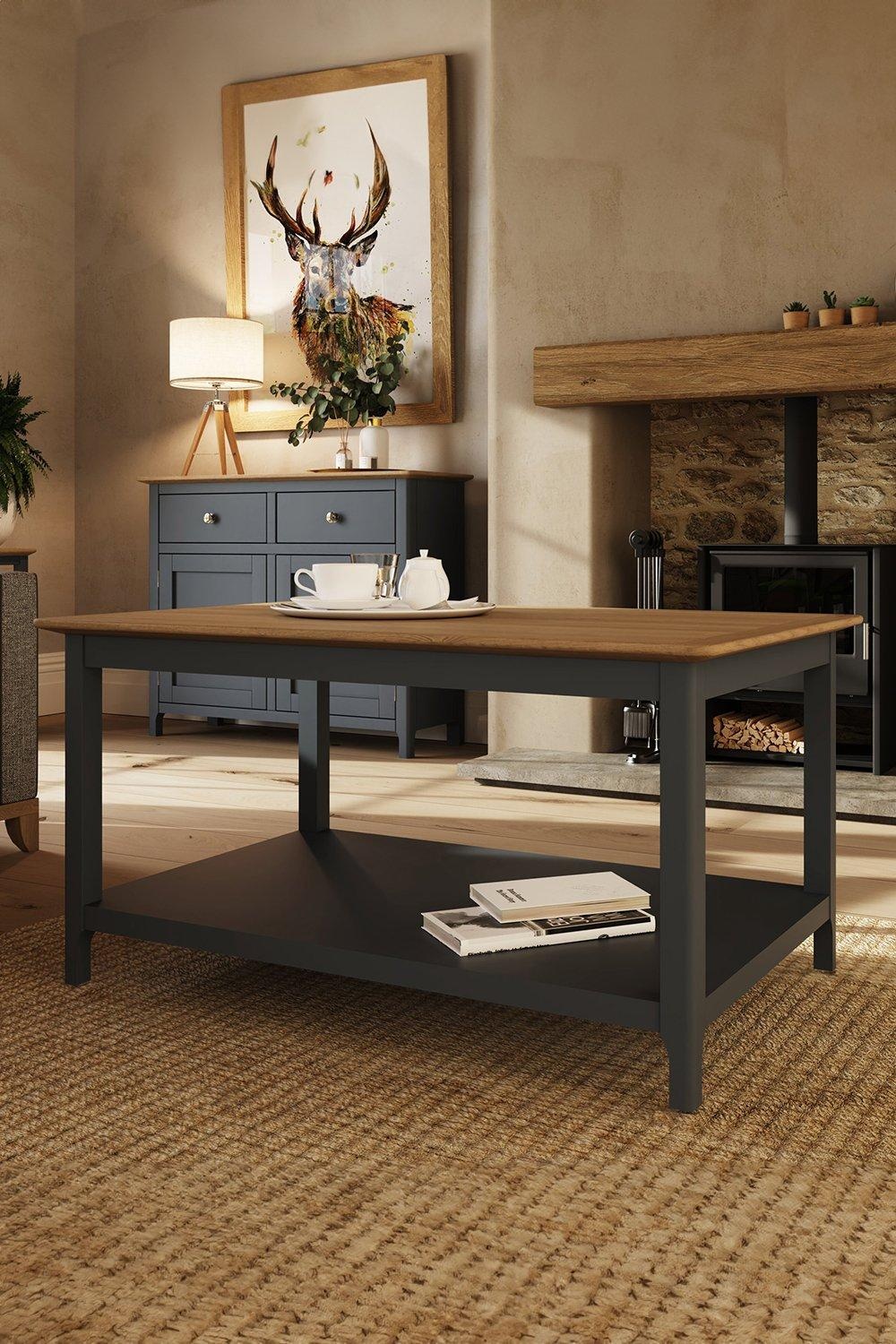 Large coffee table featuring a graphite blue painted oak veneer base and a natural wood top, with a lower shelf for storage, set in a cozy living room environment.