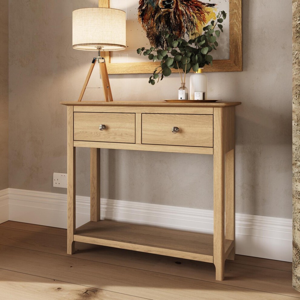 Solid oak console table in natural finish featuring two drawers, a lower shelf, and a minimalist design, complemented by a lamp and decorative items on top.
