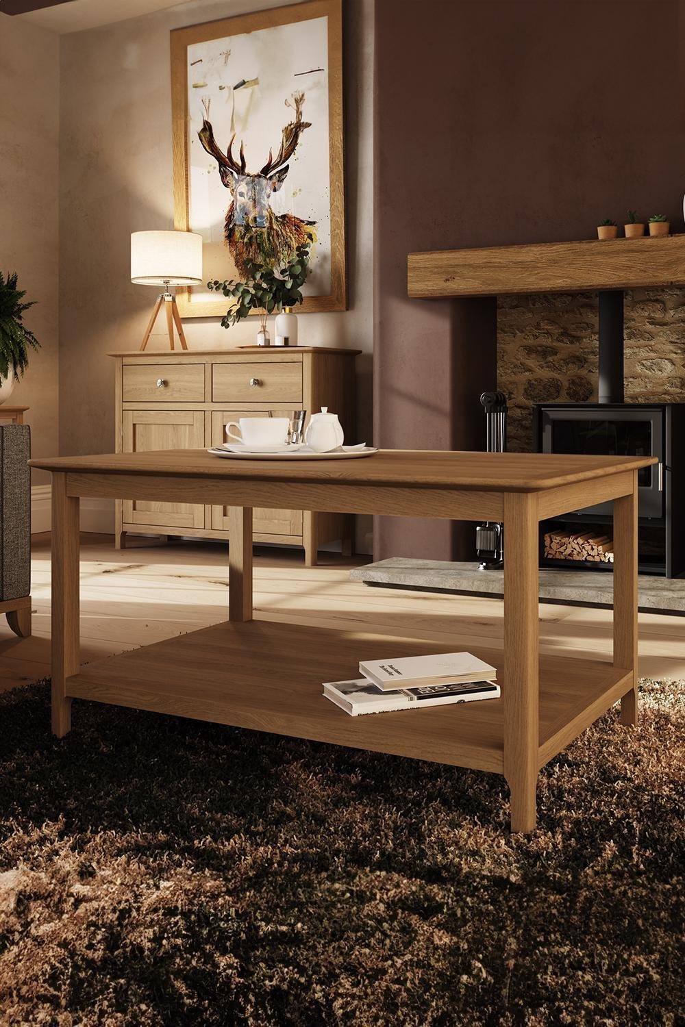 Solid oak coffee table in natural brown finish, featuring a clean design with a lower shelf, set in a cozy living room with warm lighting and decorative elements.