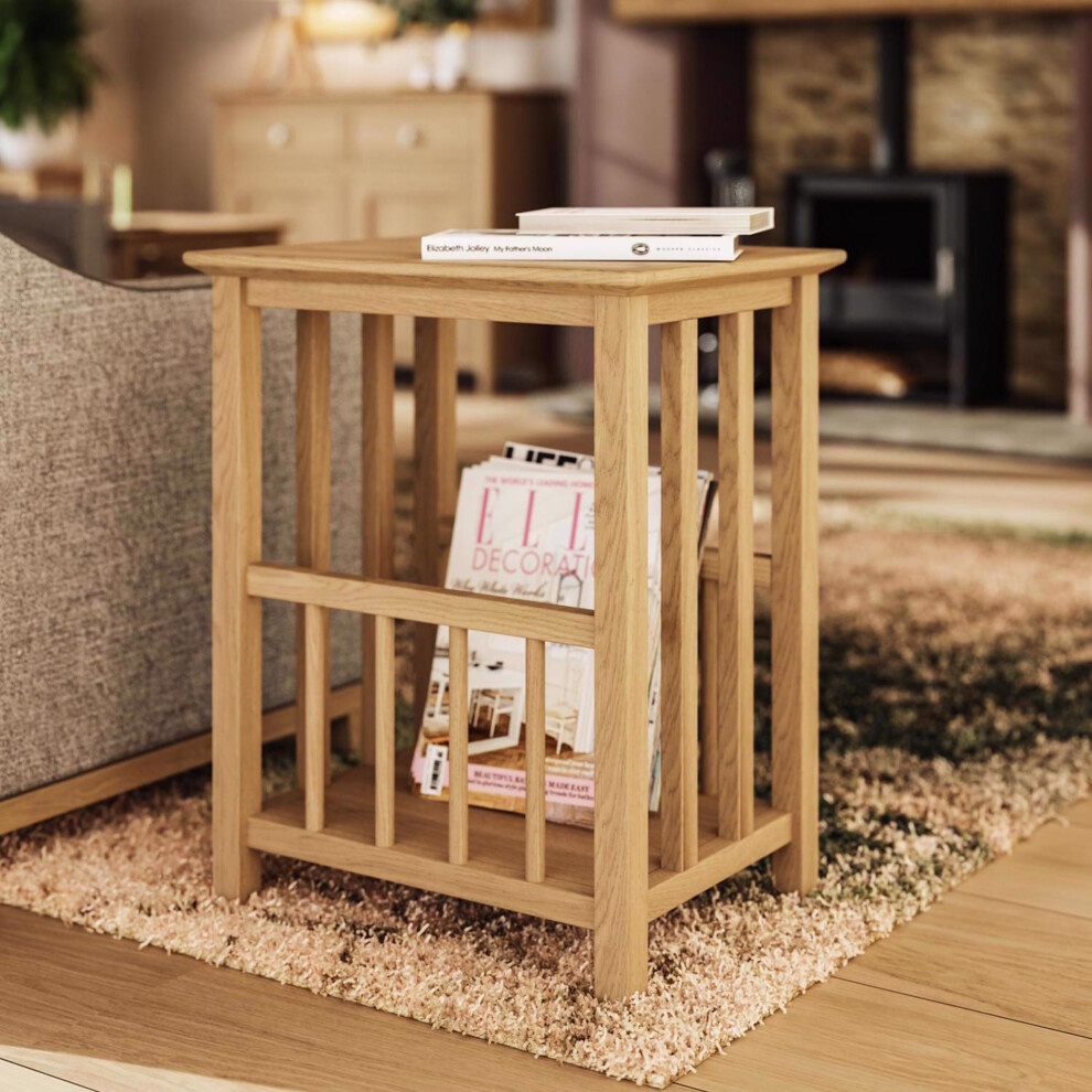 Natural oak veneer magazine rack with a slatted design, featuring an open shelf for storage, placed beside a sofa on a plush rug in a cozy living room setting.