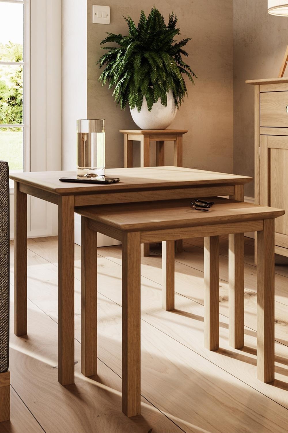 Natural solid oak nest of two tables featuring a light wood finish, clean lines, and minimalist design, set in a bright room with a potted plant and glass of water on the larger table.