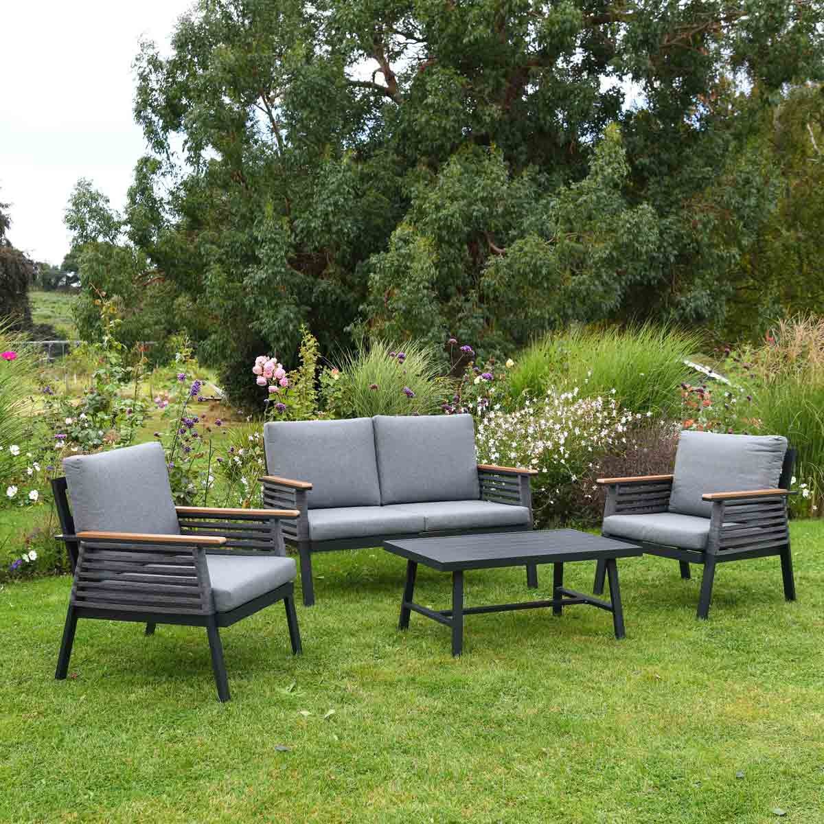 Four-piece outdoor furniture set featuring grey cushions, aluminum frames, and wooden armrests, arranged on a lawn surrounded by flowers and greenery.