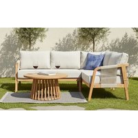 Acacia wood corner sofa set with beige cushions, blue accent pillow, and round slatted coffee table on grass.