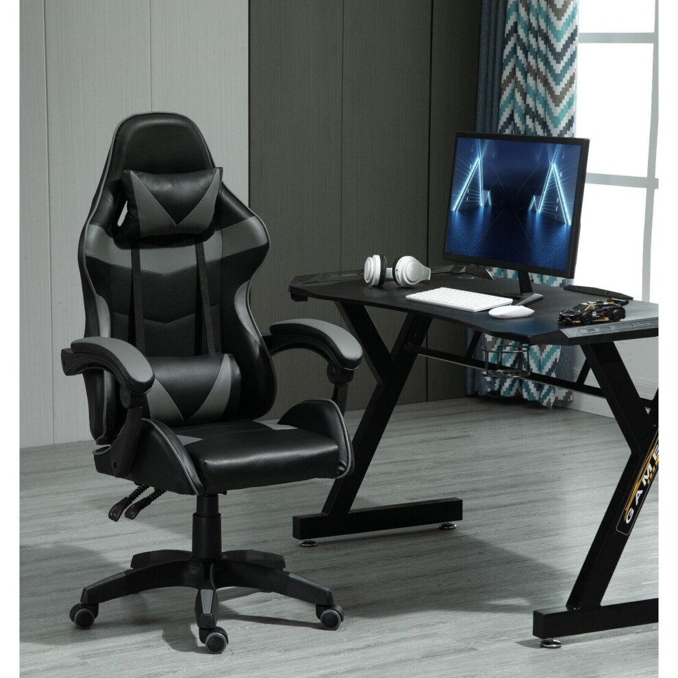 Grey and black gaming chair with a high back, padded seat, adjustable armrests, tilt and swivel functions, positioned next to a sleek black desk and monitor.