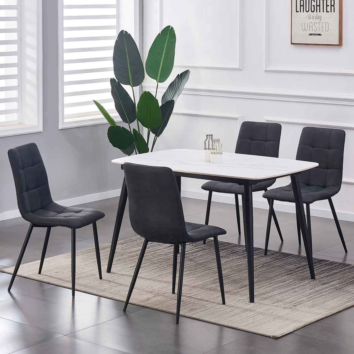 Set of four black faux suede leather dining chairs with a tufted design, paired with a white rectangular table and surrounded by a light-colored rug and indoor plants.