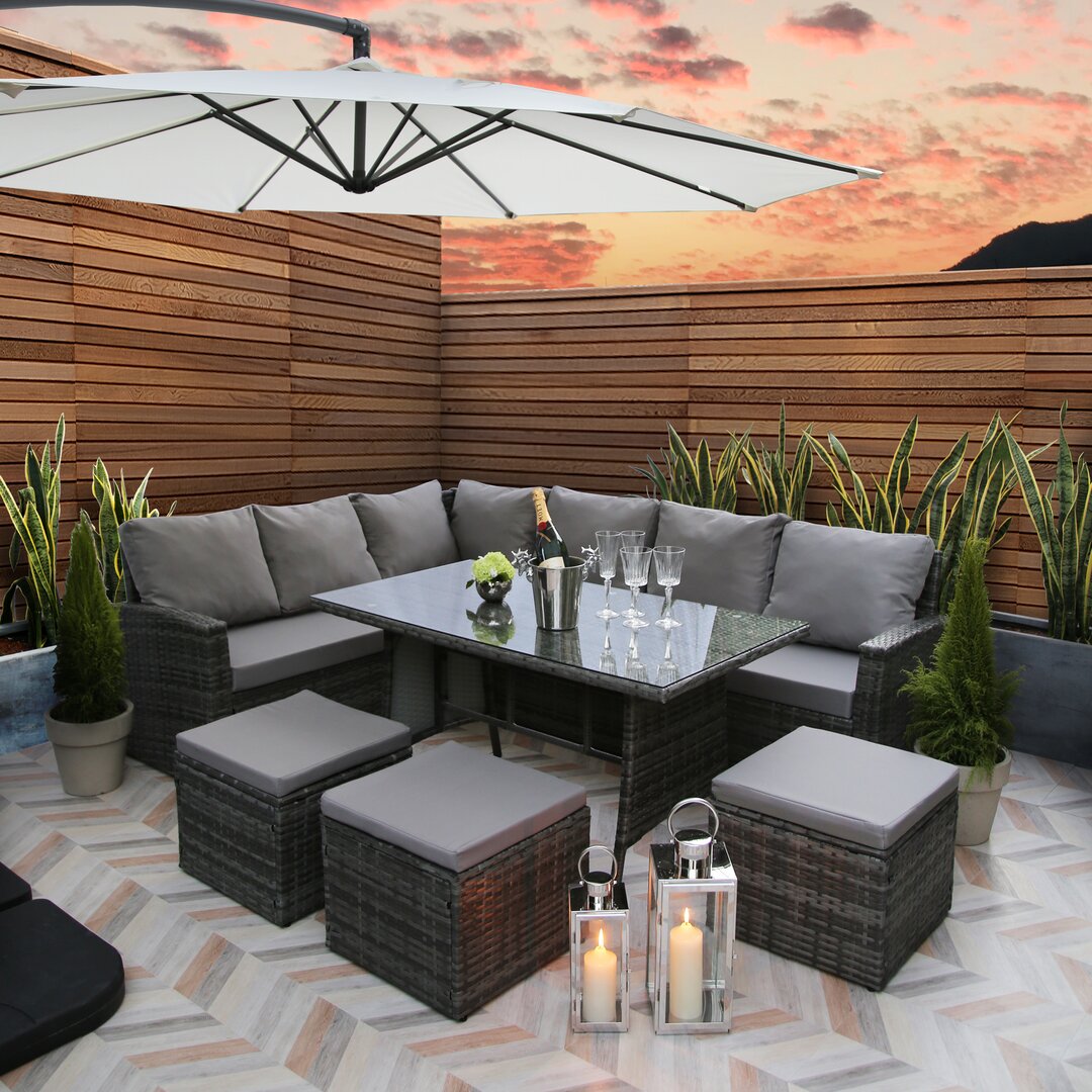 Stylish 8-seater lounge set with a glass-top table, grey cushions, and dark wicker seating, complemented by an umbrella and decorative lanterns in a cozy outdoor setting.
