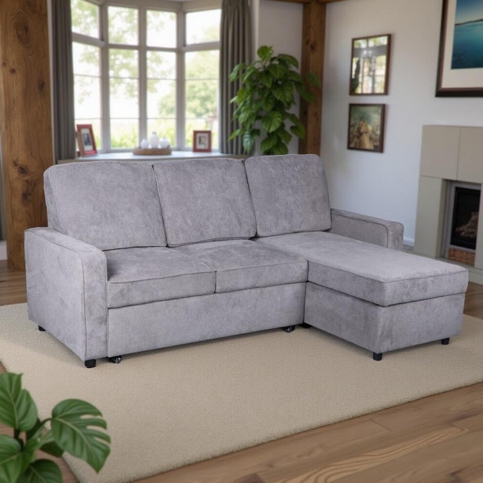 Gray upholstered sectional corner sofa with a pull-out bed feature, featuring a spacious chaise lounge and modern design, set in a bright room with large windows.