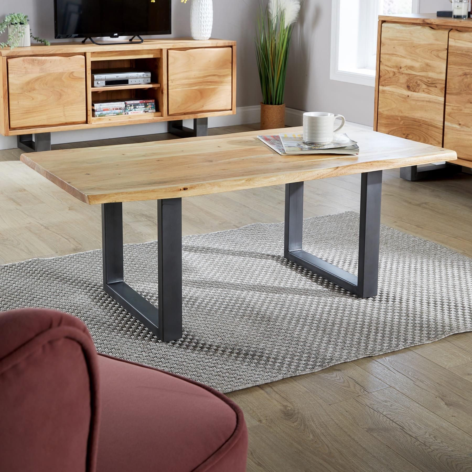 Live edge coffee table featuring a solid 26mm acacia wood top with natural grain patterns and black metal legs, set on a textured rug in a modern living room.